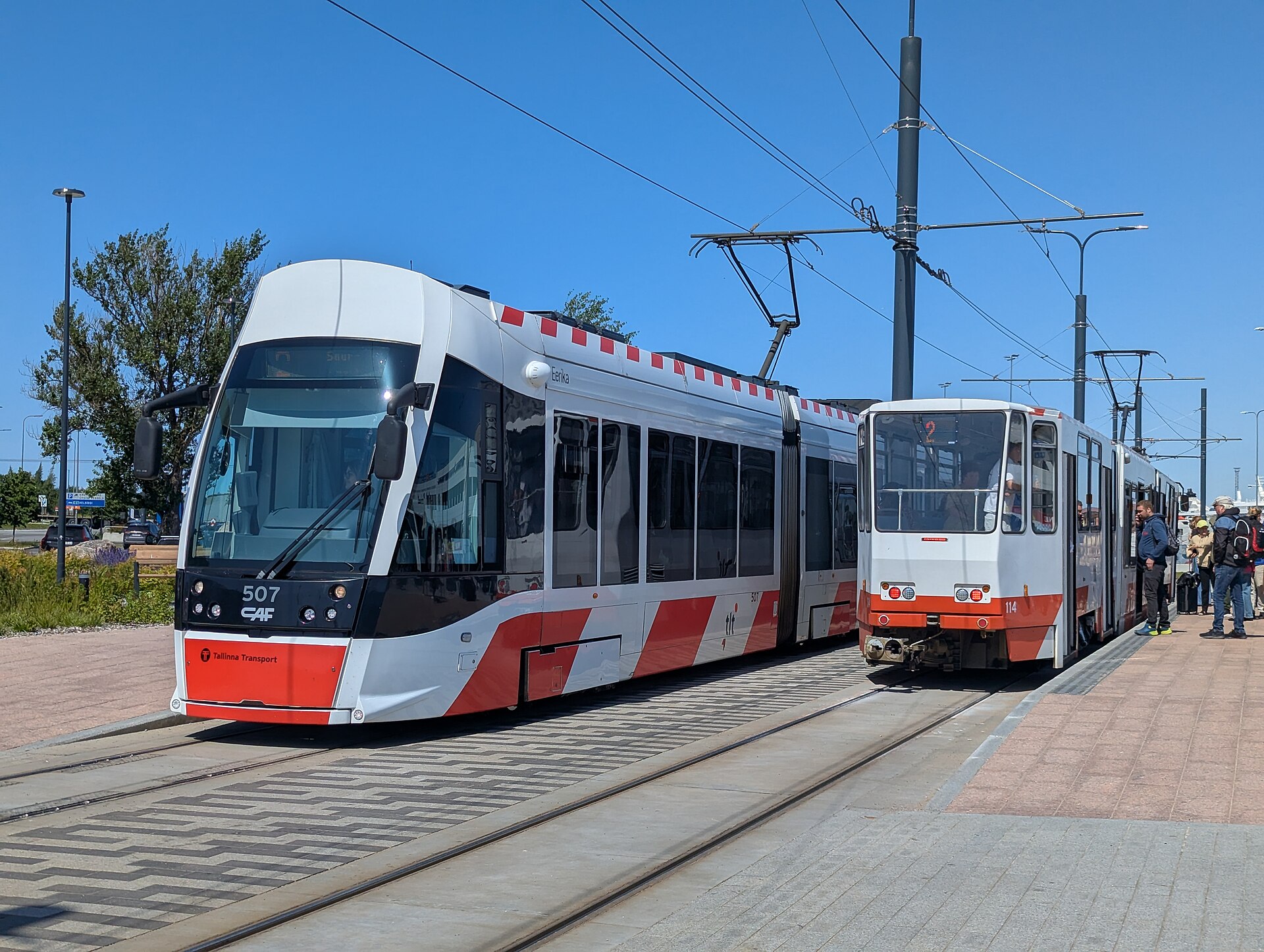 Dve električky stoja na konečnej zastávke, vpravo skupina čakajúcich cestujúcich