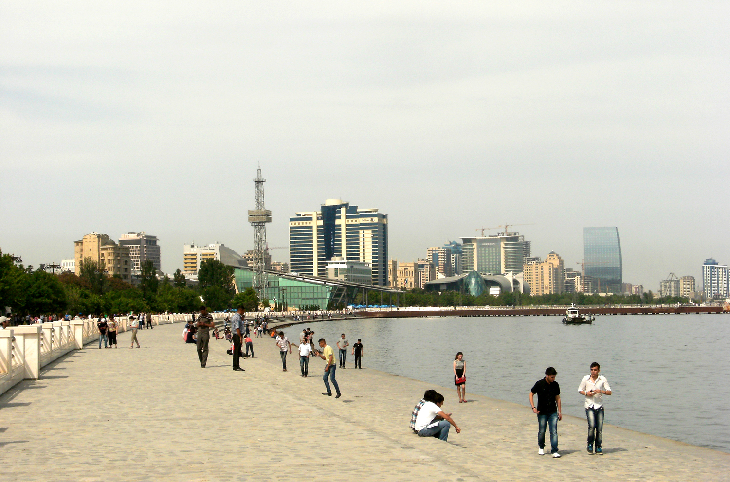 Ľudia sa prechádzajú po pobrežnej promenáde v Baku, v pozadí výškové budovy