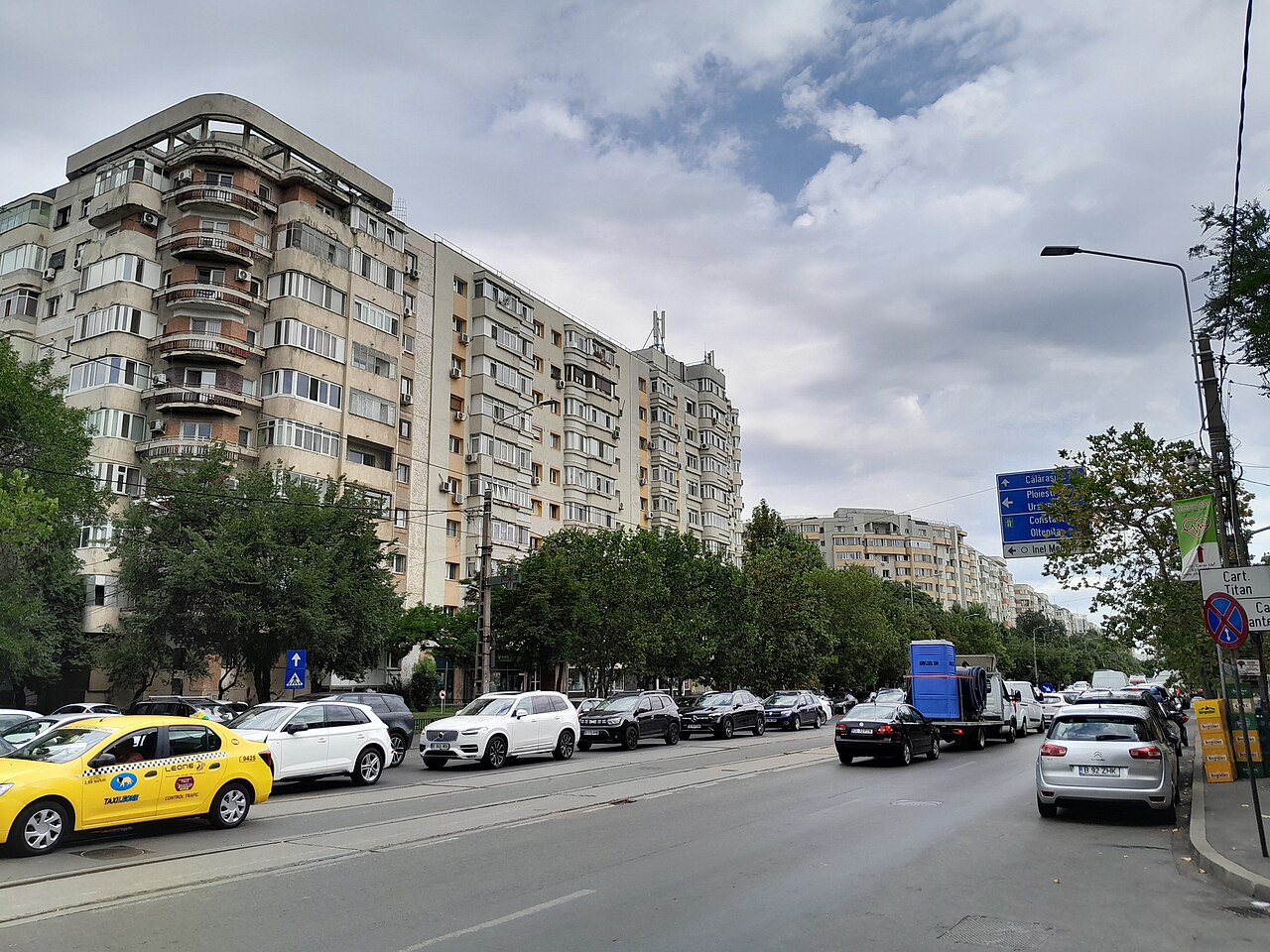 Mestská trieda s panelovými domami, žltými taxíkmi a zaparkovanými autami