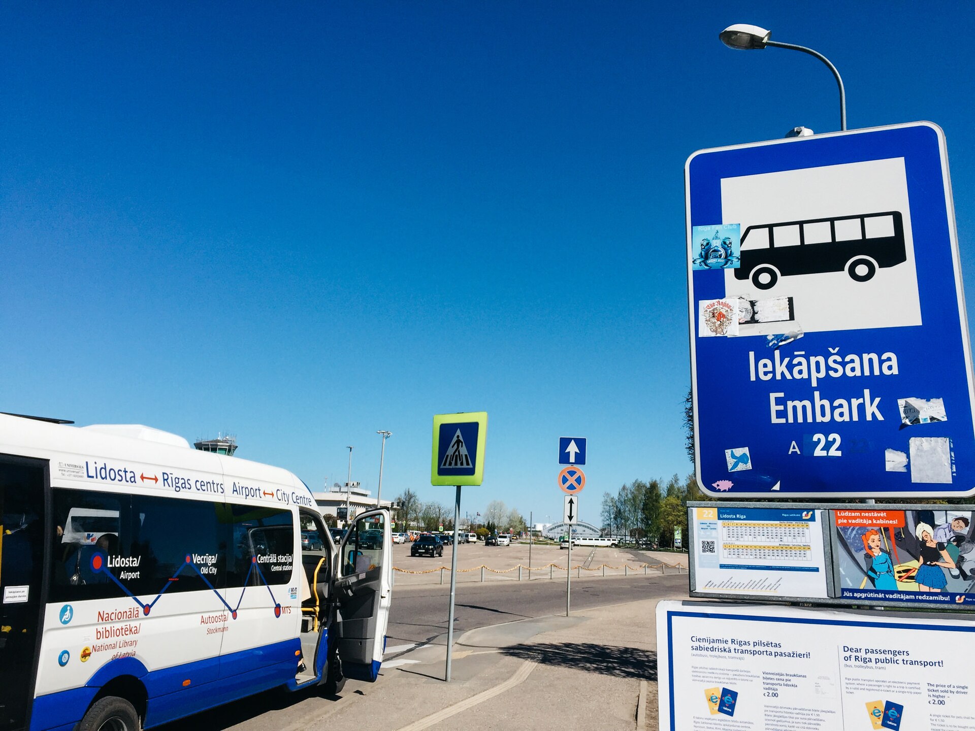 Nízkopodlažný mestský autobus stojí pri zastávke na parkovisku letiska, vedľa neho modrý stĺpik so symbolom autobusu a číslom 22
