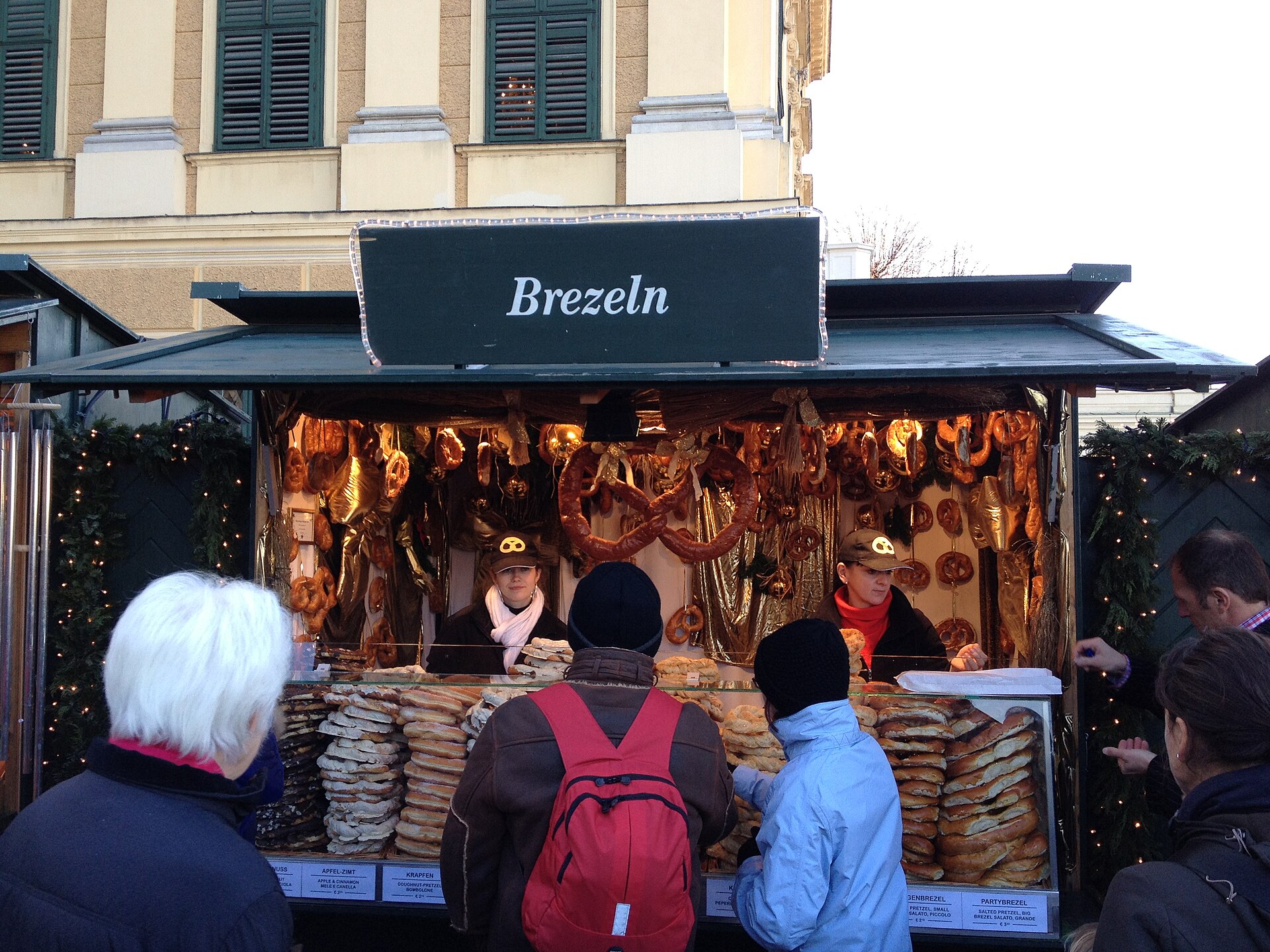 Stánok s preclíkmi na vianočnom trhu, pred ním stoja traja návštevníci v zimných bundách