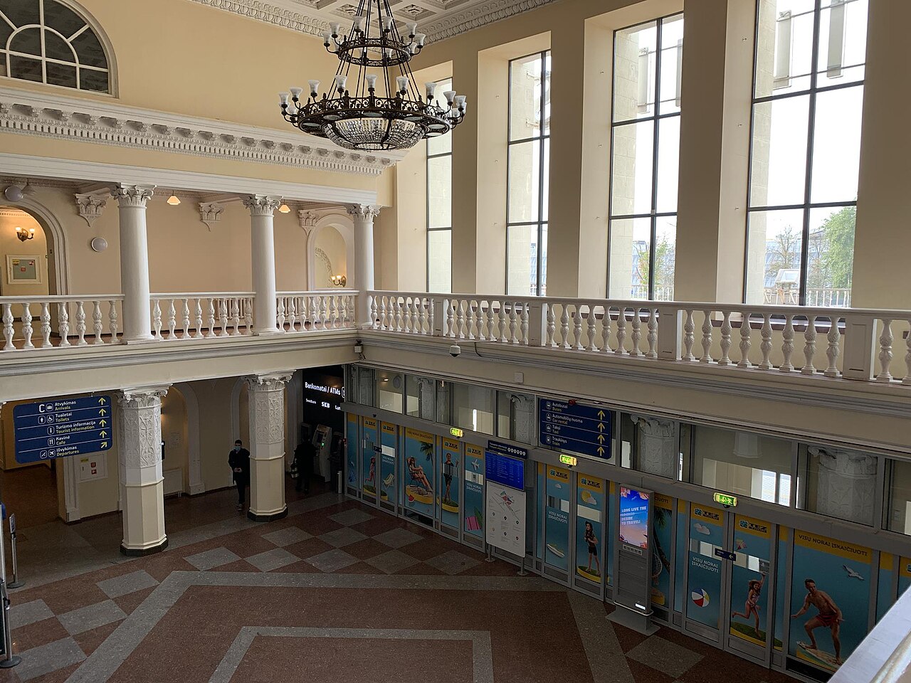 Odbavovacia hala v historickej letiskovej budove s bielymi stĺpmi, balustrádou a lustrom